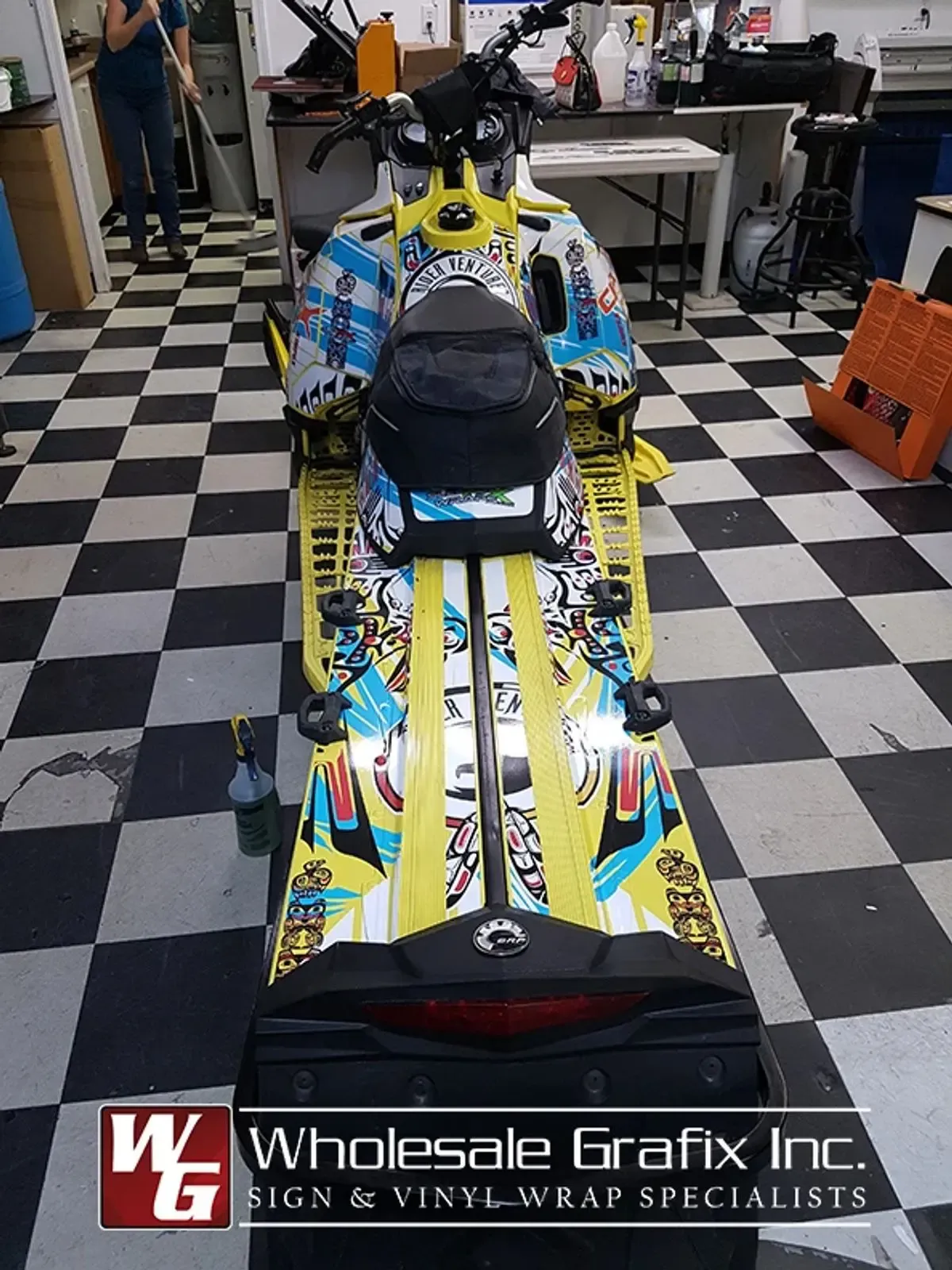 Yellow and blue wrapped snowmobile on the shop checkerboard floor