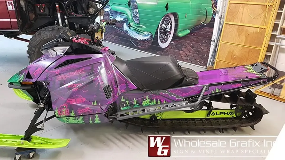 Snowmobile wrapped in a purple and green treeline design